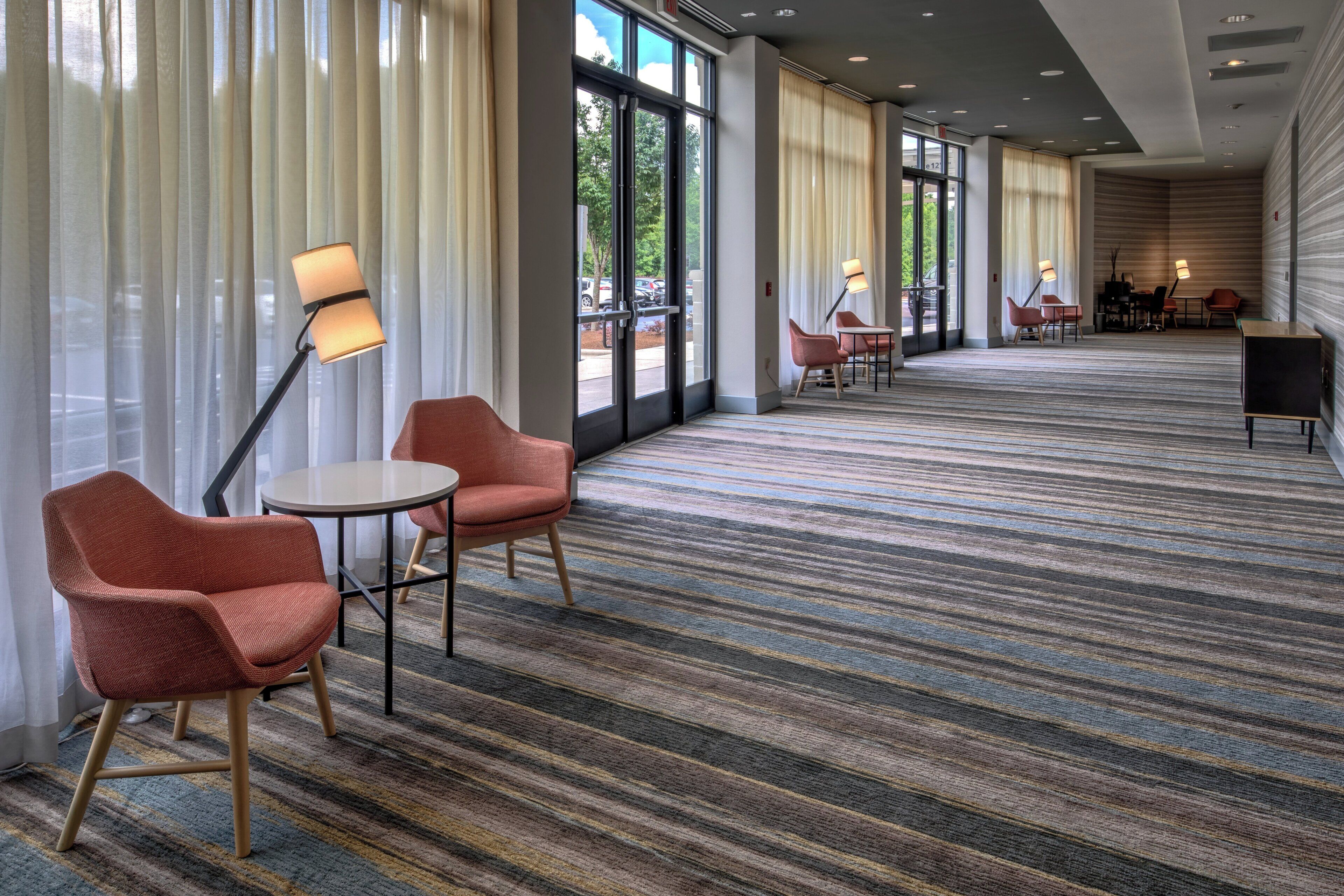 Un vestíbulo de hotel con alfombra a rayas, zonas de estar y ventanas amplias.
