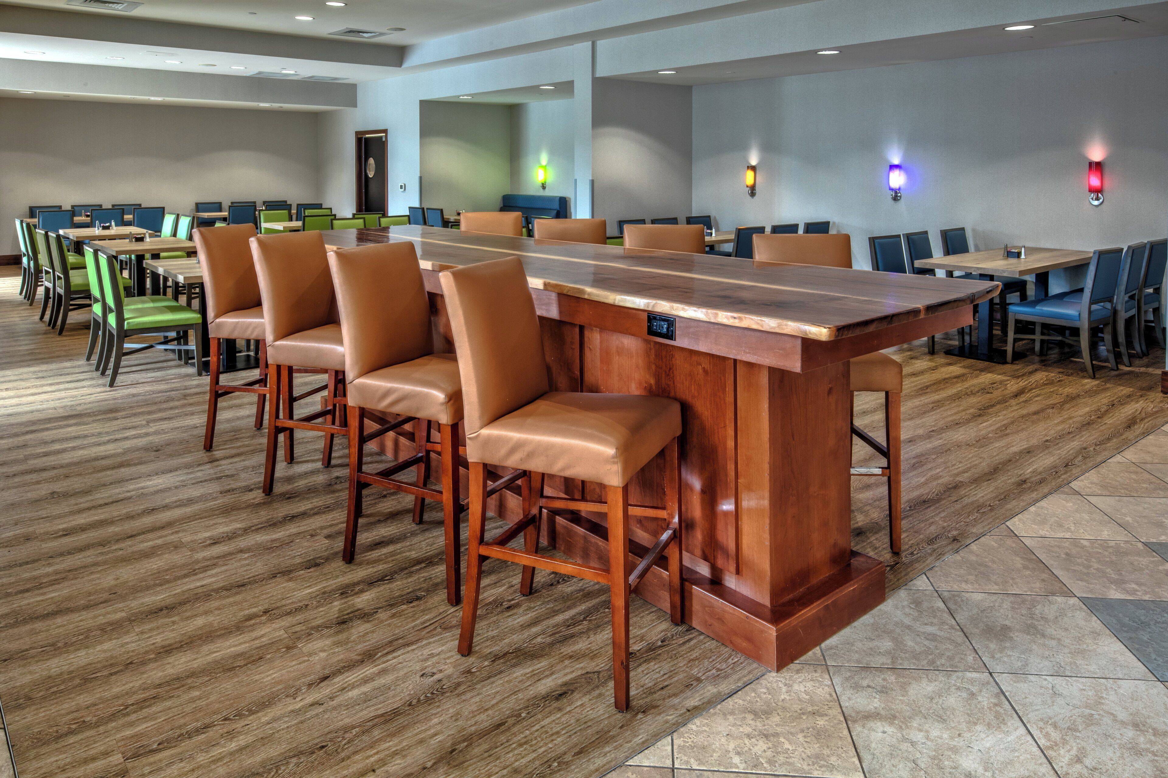 Un salón de conferencias con una larga mesa de madera y varias sillas, suelo de baldosas y una puerta al fondo.