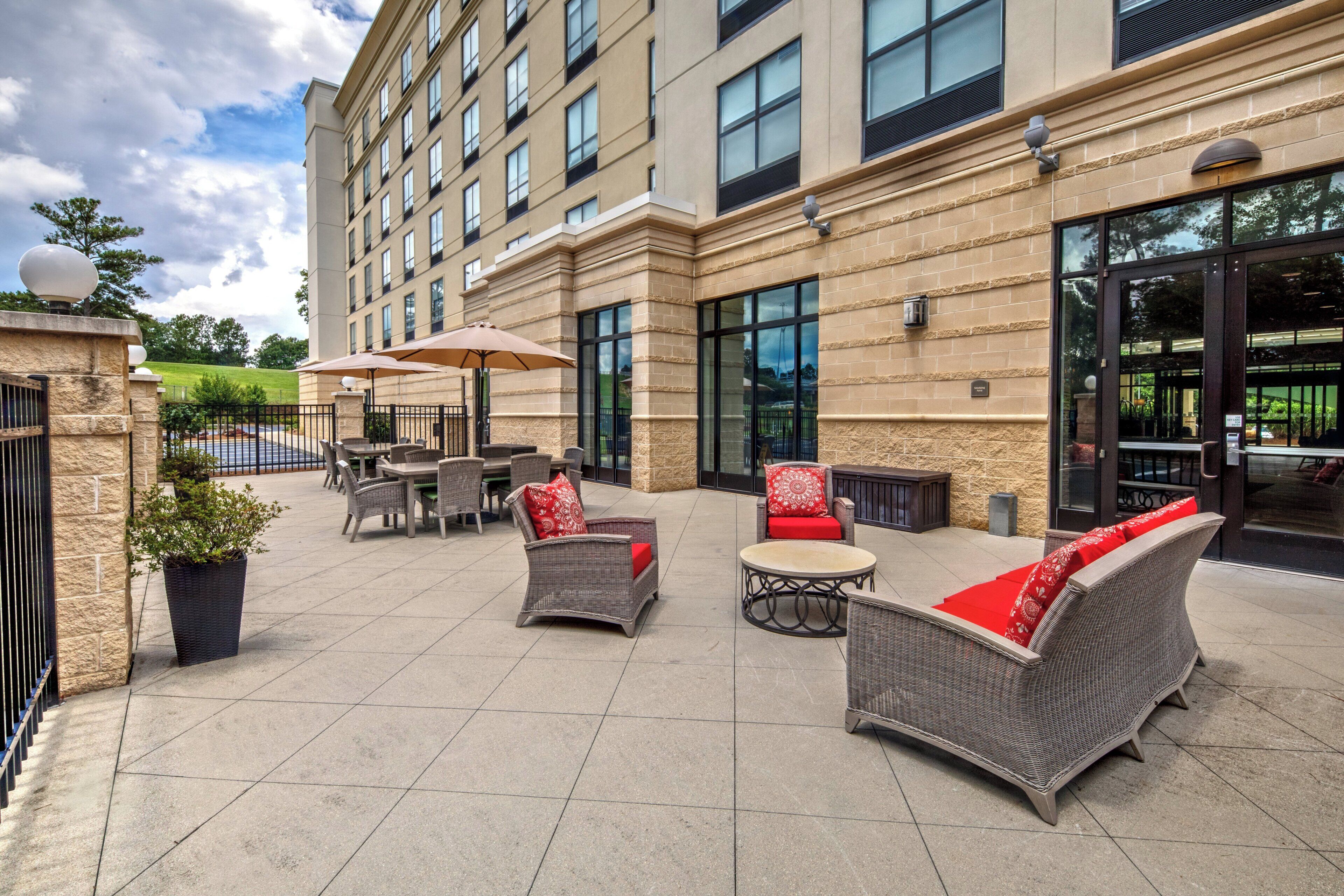 A hotel patio with outdoor seating, a stone facade, and large windows.