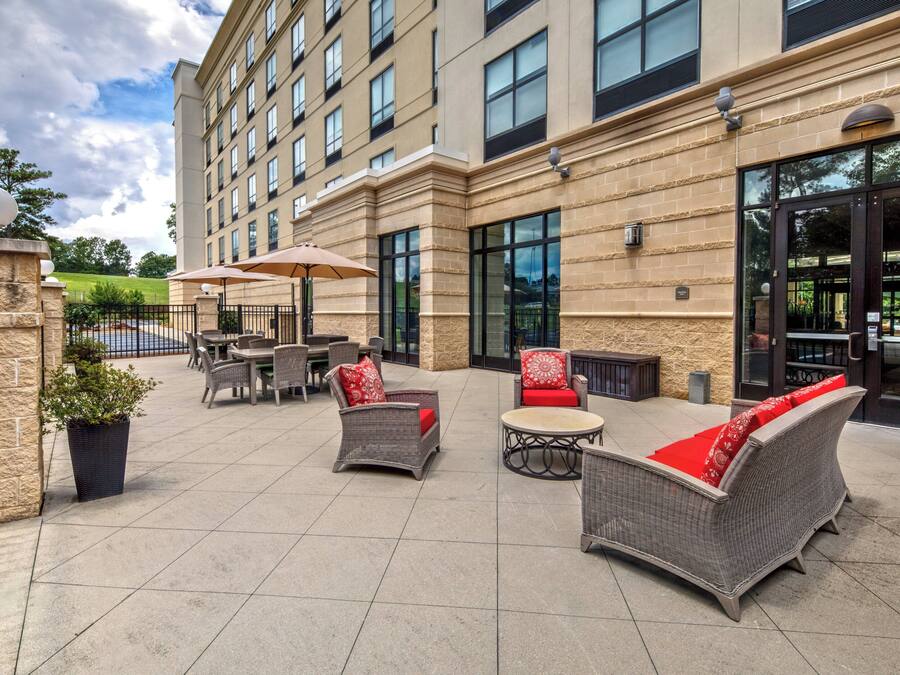 A hotel patio with outdoor seating, a stone facade, and large windows.