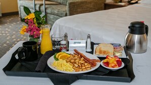 Un vassoio per la colazione con uova, pancetta, pane tostato, frutta e una caffettiera su un letto d'hotel.