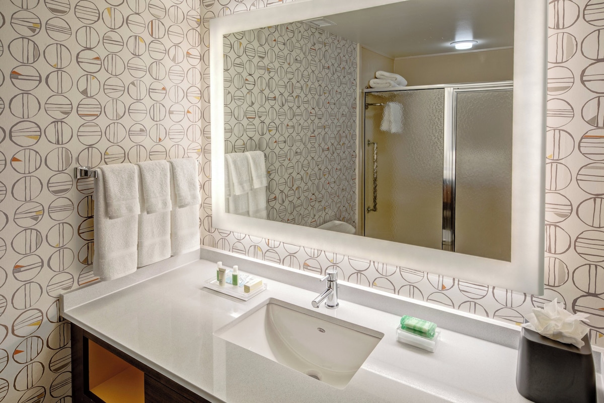 A bathroom with a large mirror, a sink, and a towel rack.