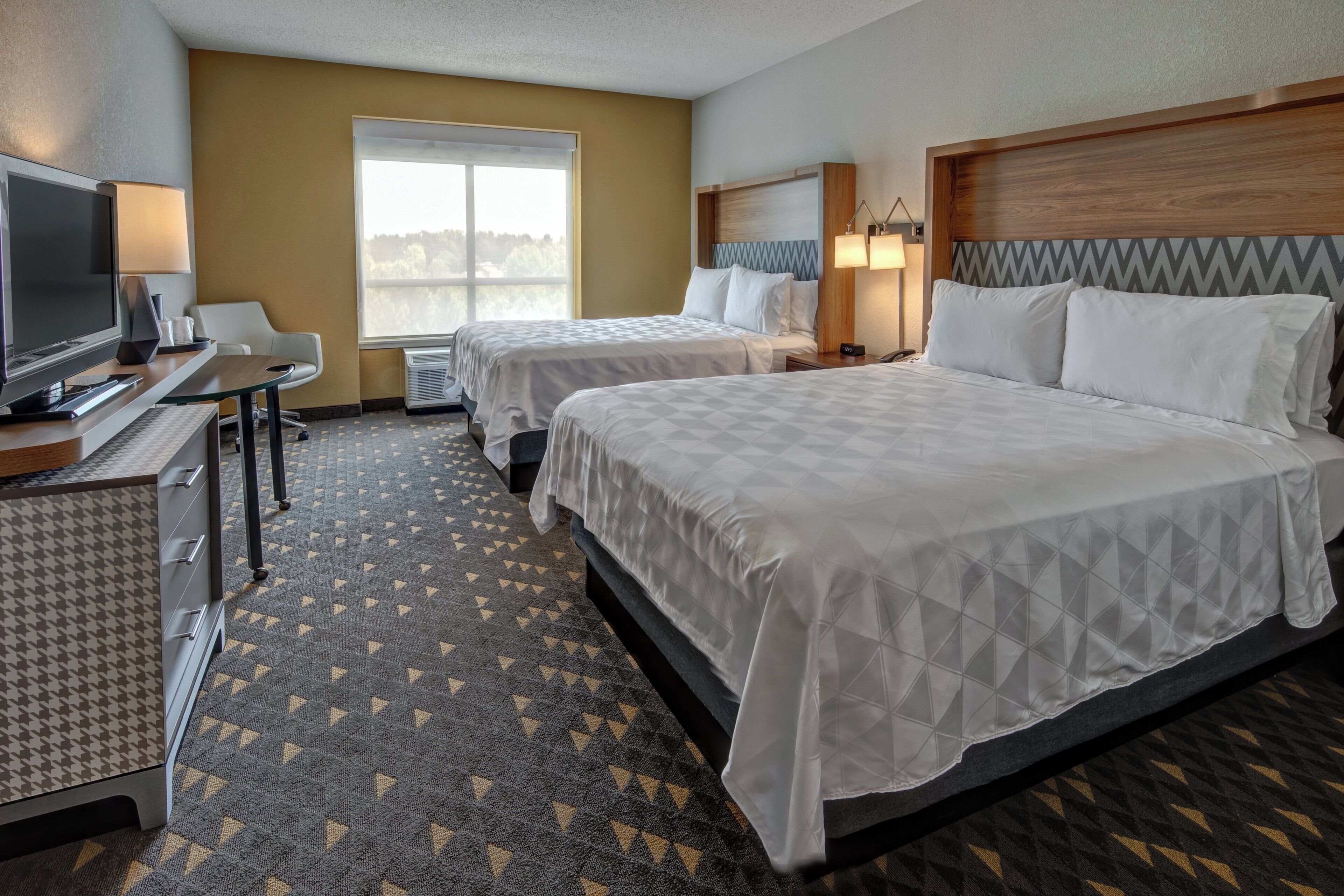 A hotel room with two beds, a desk with a TV, and a window with a view.