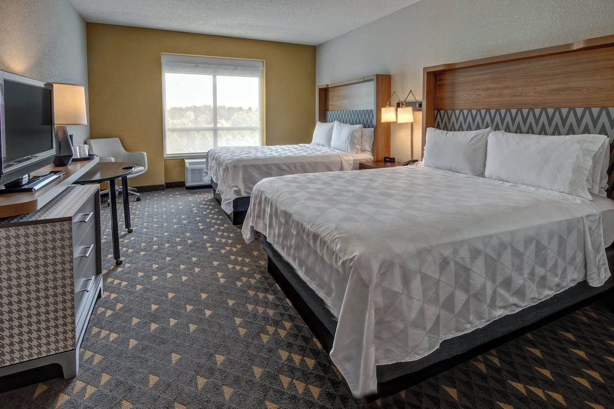A hotel room with two beds, a desk with a TV, and a window with a view.