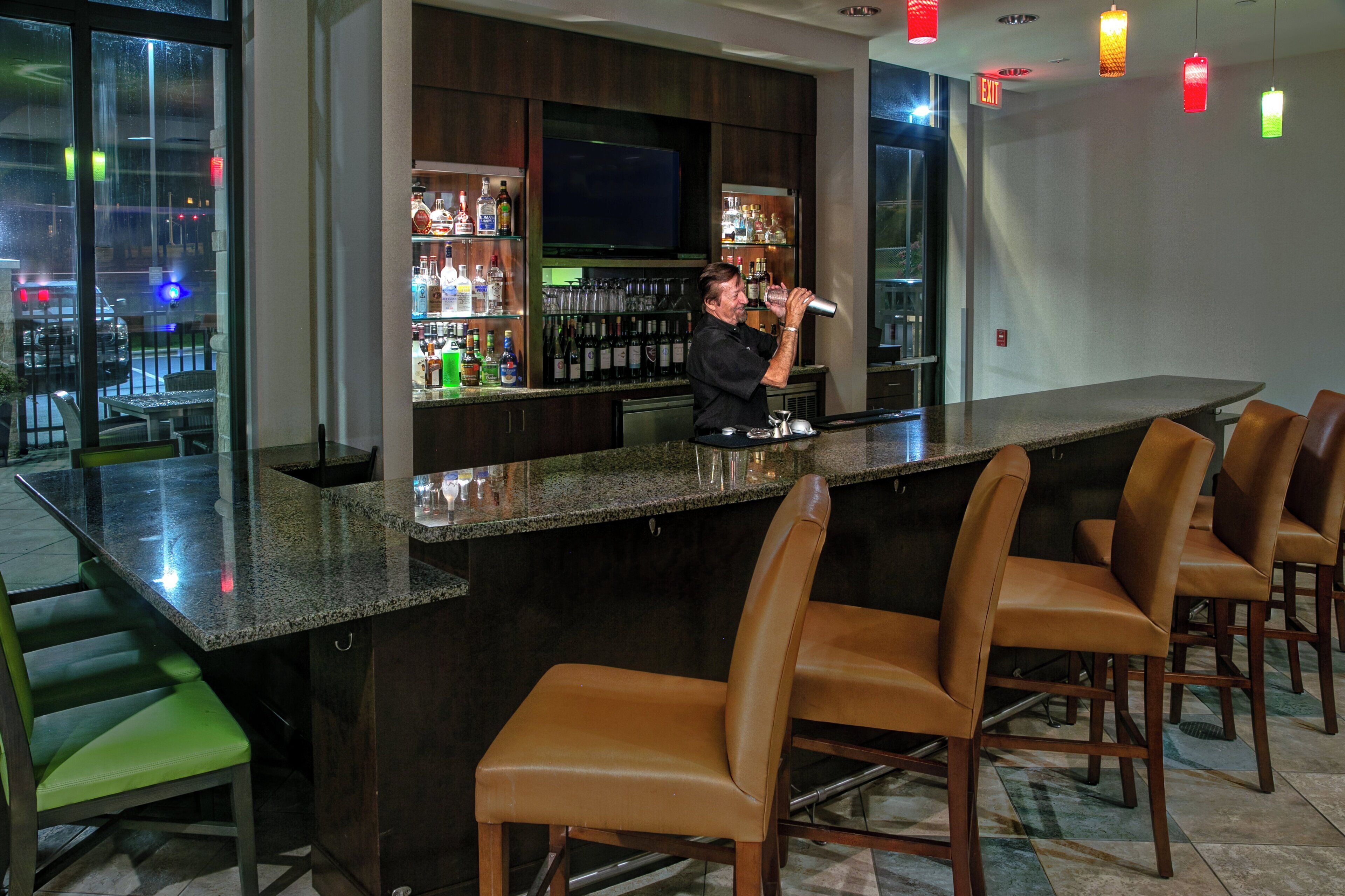 A bar area with a counter, bar stools, and a variety of bottles and glasses.