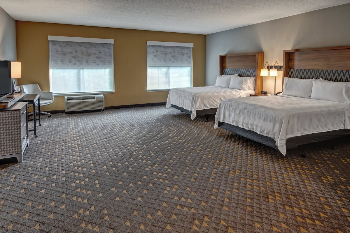 A hotel room with two beds, a desk with a chair, a TV, and a window with blinds.
