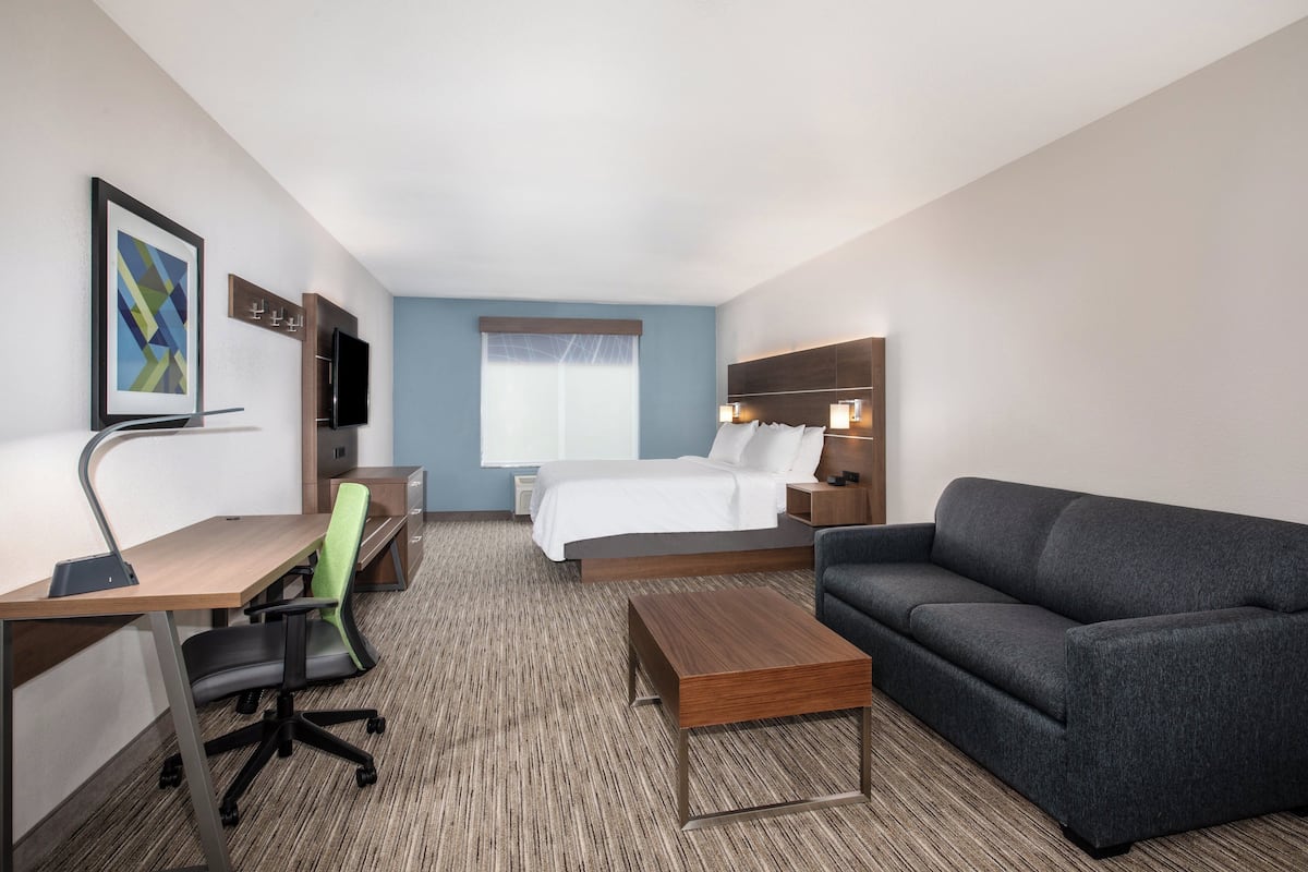 A hotel room with a bed, a desk with a chair, a sofa, a TV, and a framed picture on the wall.