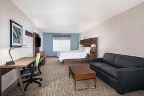 Une chambre d’hôtel comprenant un lit, un bureau avec une chaise, un canapé, une télévision et un tableau encadré au mur.