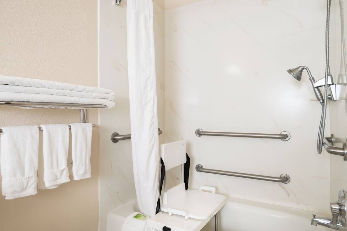 A bathroom with a bathtub, a shower, and a toilet. There are grab bars installed for safety.