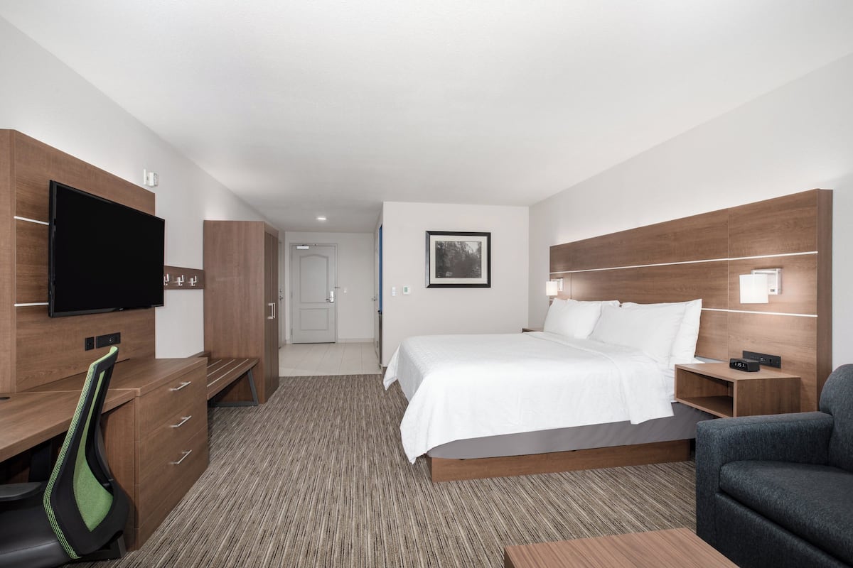 A hotel room with a bed, a desk with a chair, a television, and a picture on the wall.