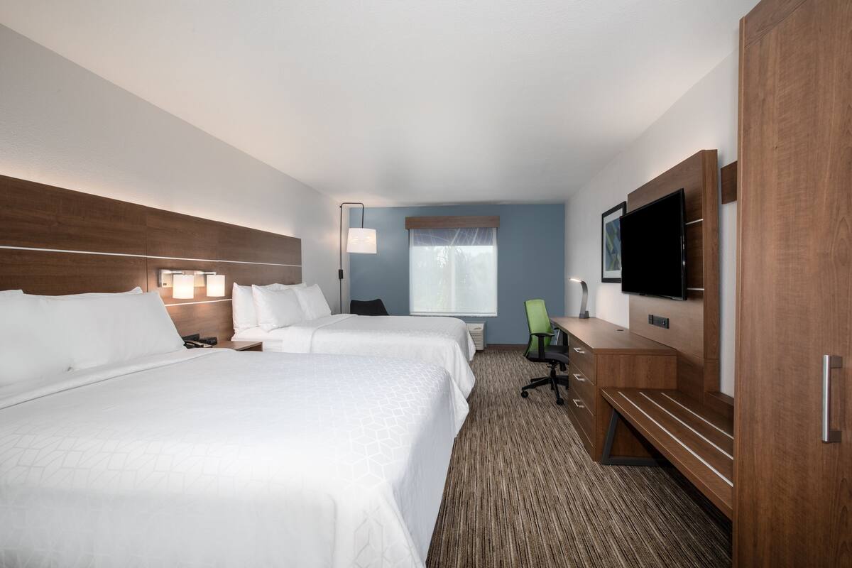 A hotel room with two beds, a desk, a chair, a TV, and a window with curtains.