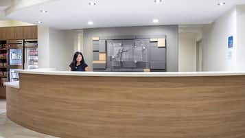 Un mostrador de recepción de hotel con diseño moderno, una pantalla digital y un cartel que indica los horarios de registro de entrada y salida.