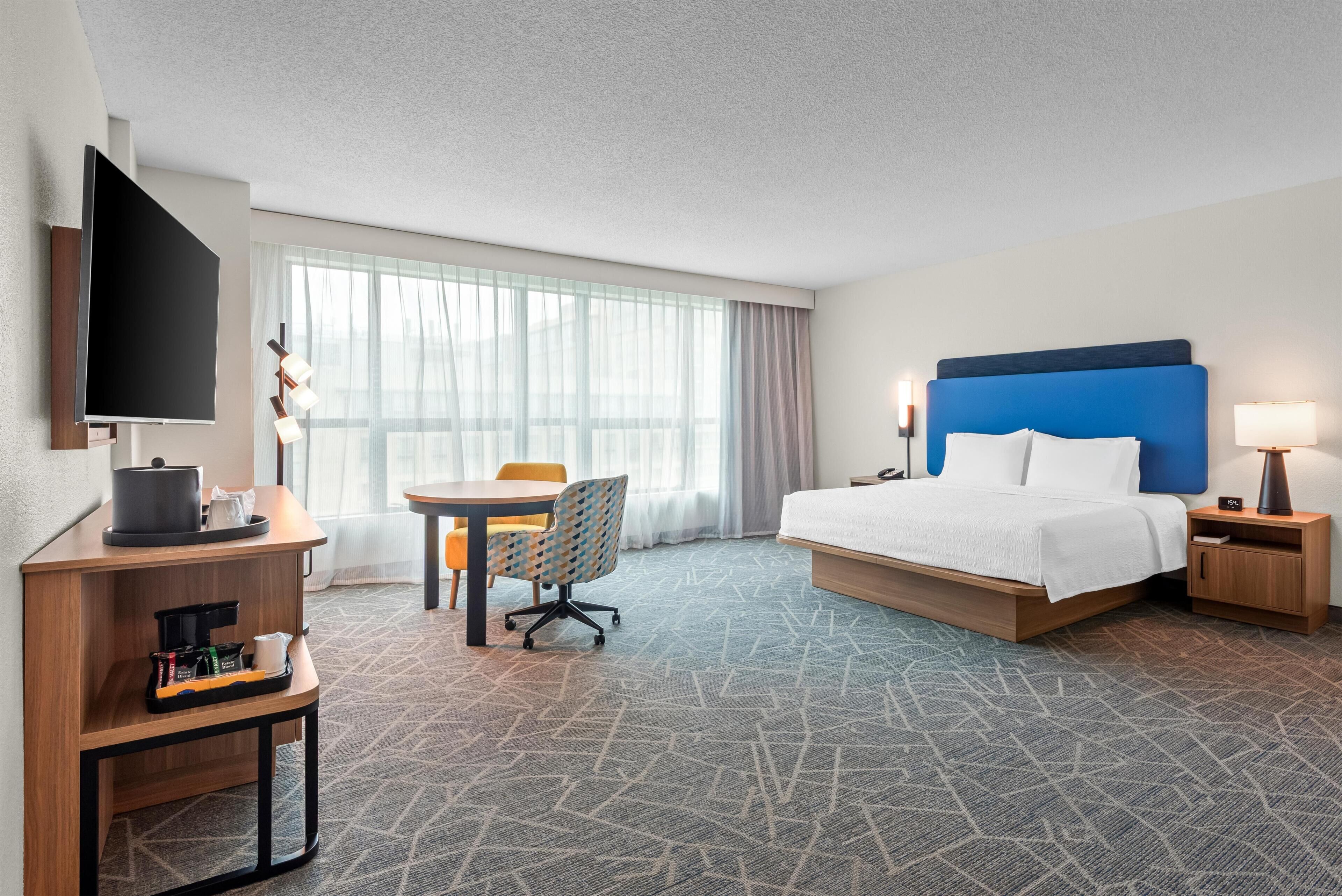 Una habitación de hotel con cama, escritorio y silla, televisión y ventana con cortinas.