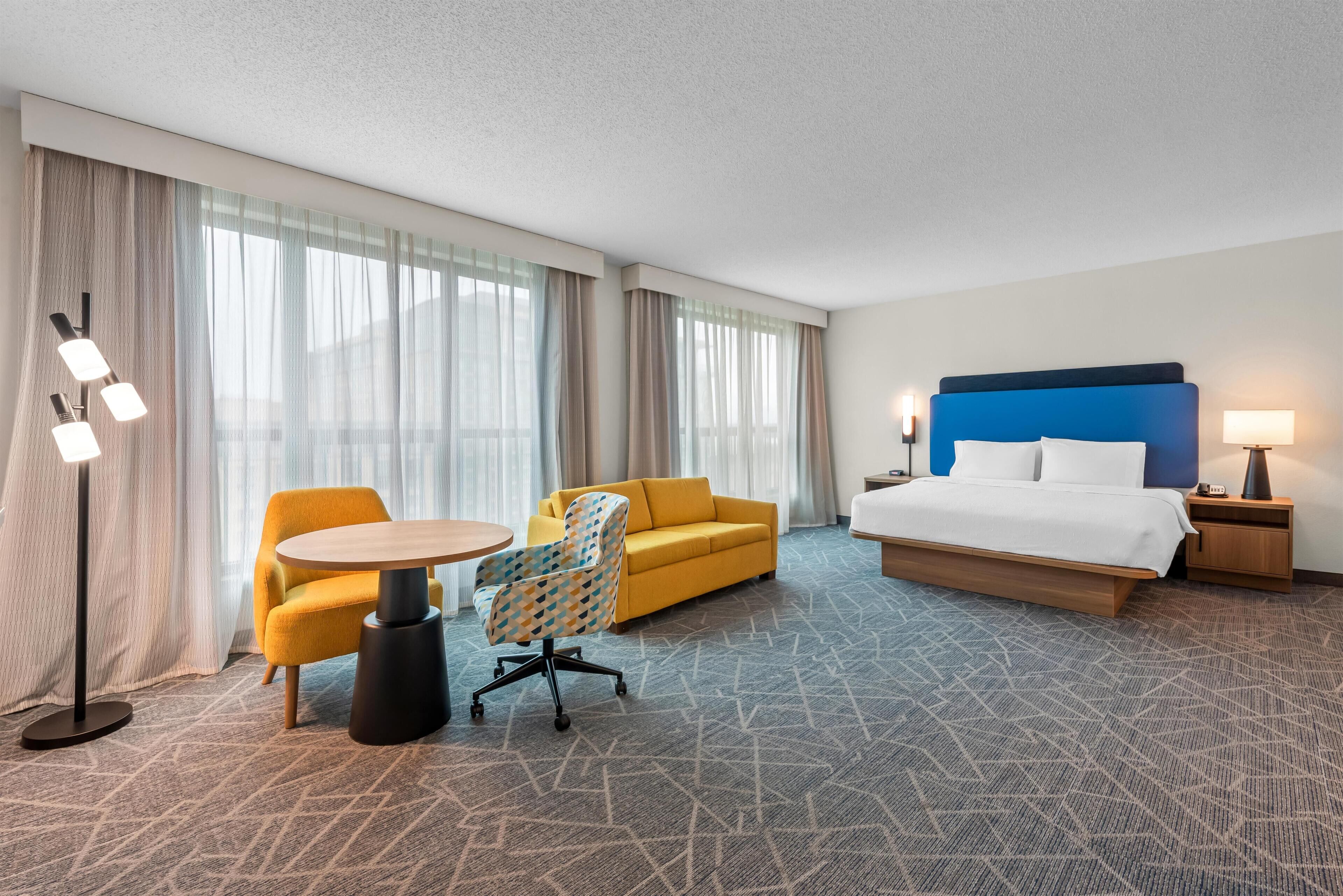 Una habitación de hotel con una cama, un sofá amarillo, una mesa redonda y una silla.