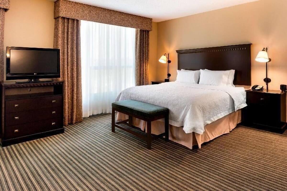 A hotel room with a bed, a television, a bench, and two bedside lamps.