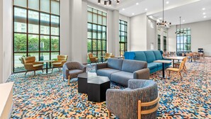 A spacious lobby with large windows, a blue sofa, patterned carpet, and modern lighting fixtures. - Hampton Inn & Suites National Harbor - Alexandria Area (Oxon Hill)