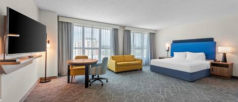 A hotel room with a bed, a desk, a sofa, a TV, and a large window.