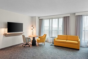 Habitación de hotel con televisión de pantalla plana, un sofá, dos sillones, una mesita redonda y una lámpara de pie.