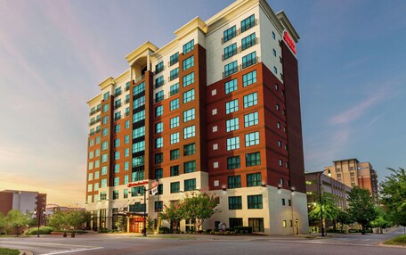 A multi-story hotel with a modern design, featuring a mix of red and beige exterior, large windows, and a prominent entrance with a flag.
