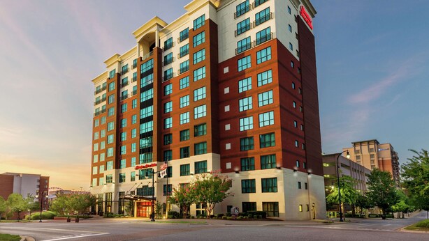 A multi-story hotel with a modern design, featuring a mix of red and beige exterior, large windows, and a prominent entrance with a flag. - Hampton Inn & Suites National Harbor - Alexandria Area (Oxon Hill)