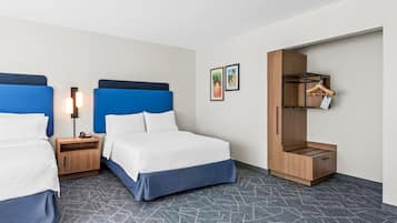 Habitación de hotel con dos camas, una mesita de noche con lámpara, un armario y suelo cubierto de alfombra.