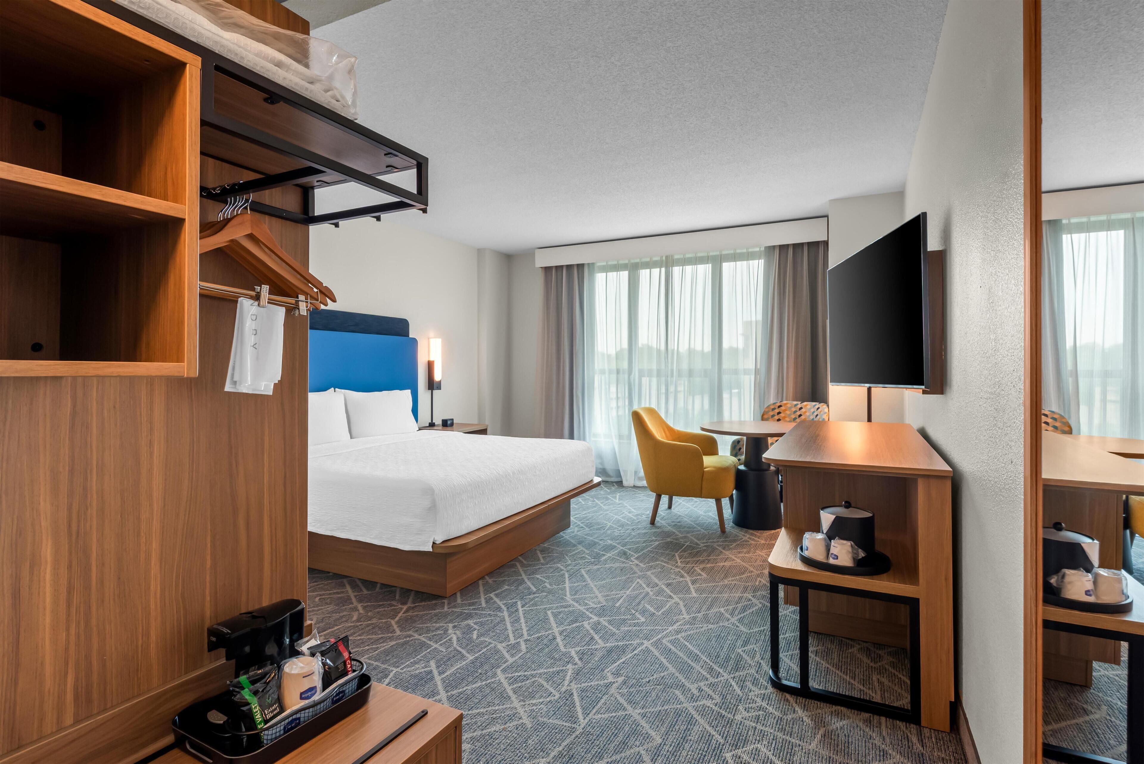 A hotel room with a bed, a desk, a chair, a TV, and a window with curtains.