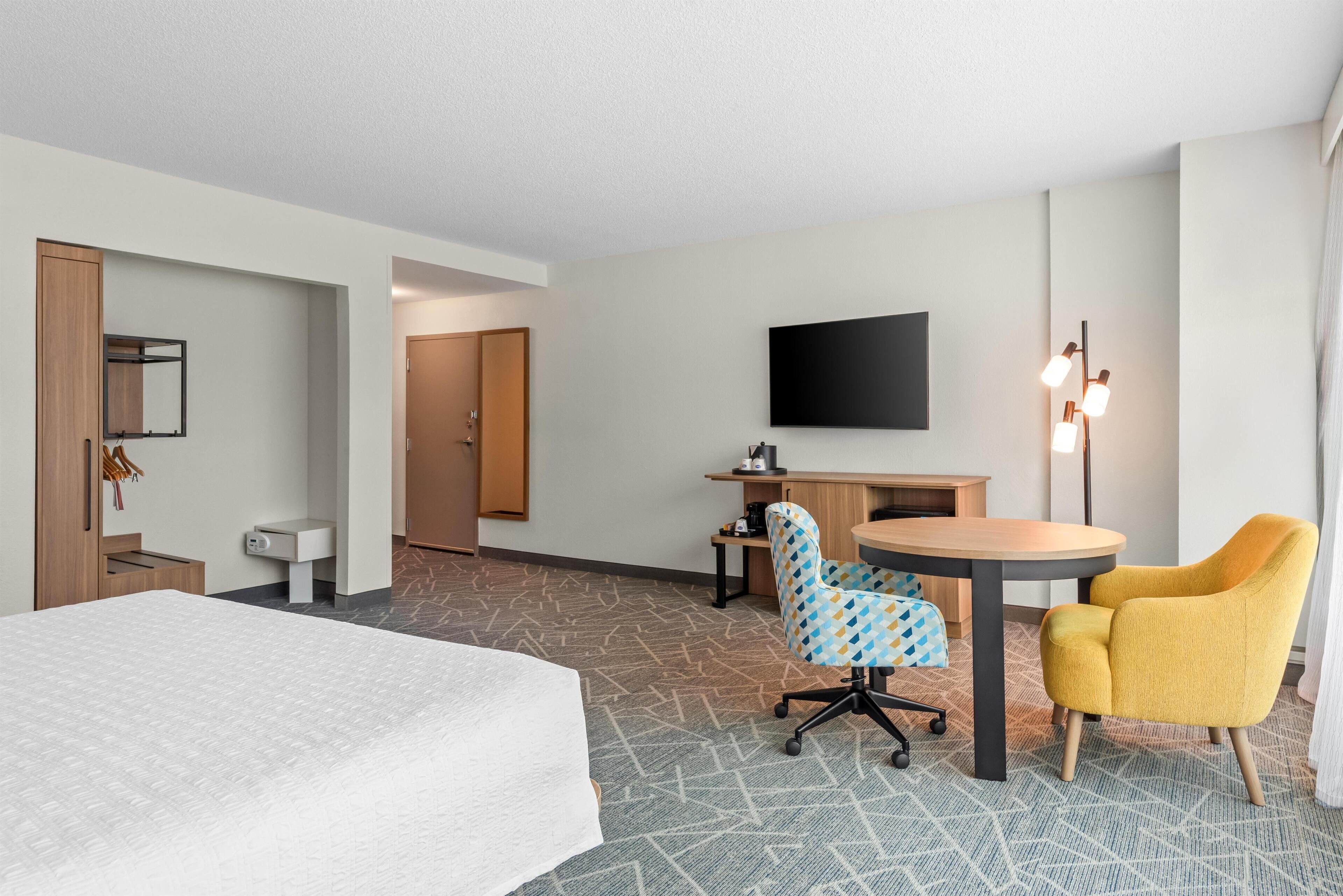 A hotel room with a bed, a desk, a chair, a television, and a lamp.