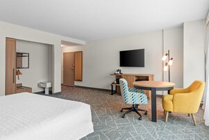 Una habitación de hotel con cama, escritorio, silla, televisor y lámpara.