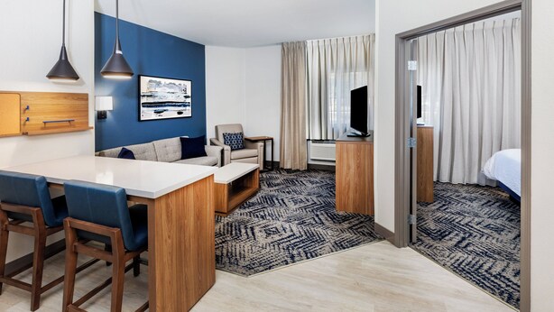 A modern hotel room with a kitchenette, a sofa, a TV, and a bed.