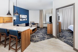 A modern hotel room with a kitchenette, a sofa, a TV, and a bed. - Candlewood Suites Fayetteville – University of Arkansas by IHG (Fayetteville)