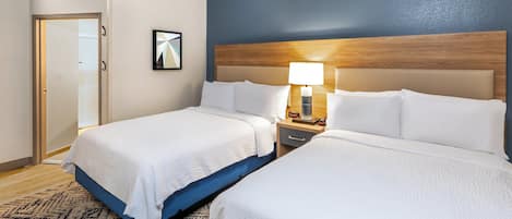 A hotel room with two beds, a wooden headboard, a nightstand with a lamp, and a framed picture on the wall.