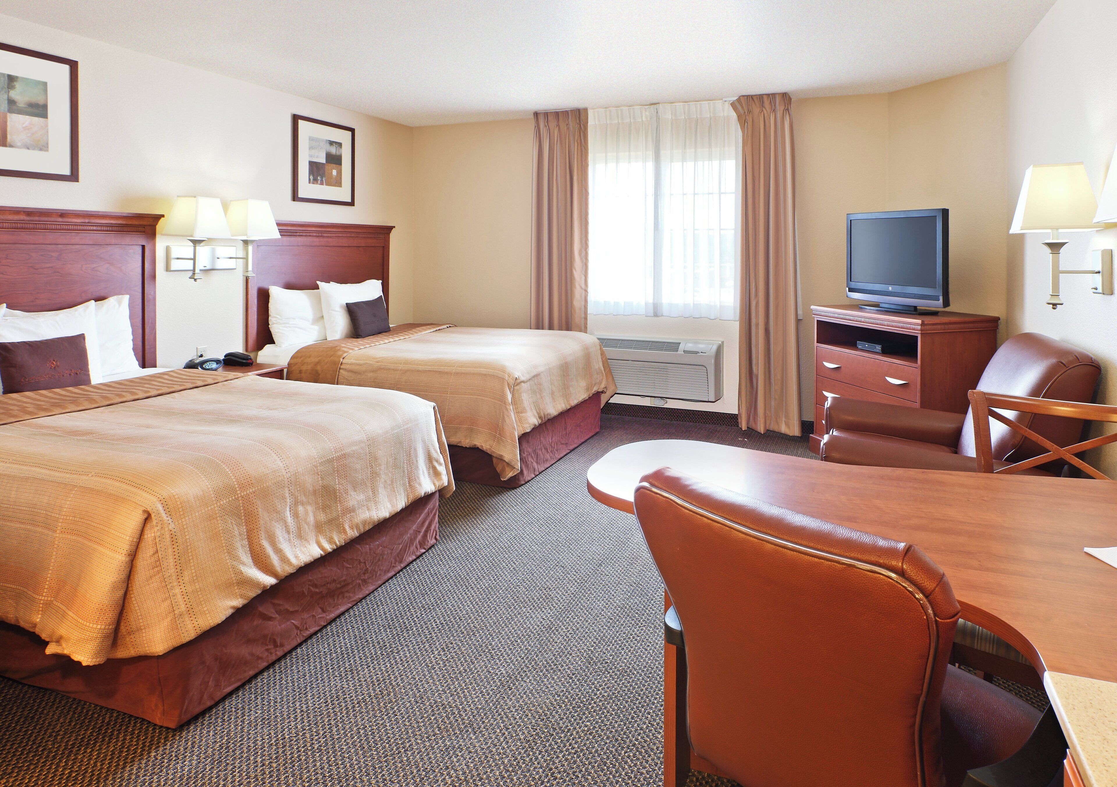 Ein Hotelzimmer mit zwei Betten, einem Schreibtisch, einem Sessel, einem Fernseher und einer Klimaanlage.