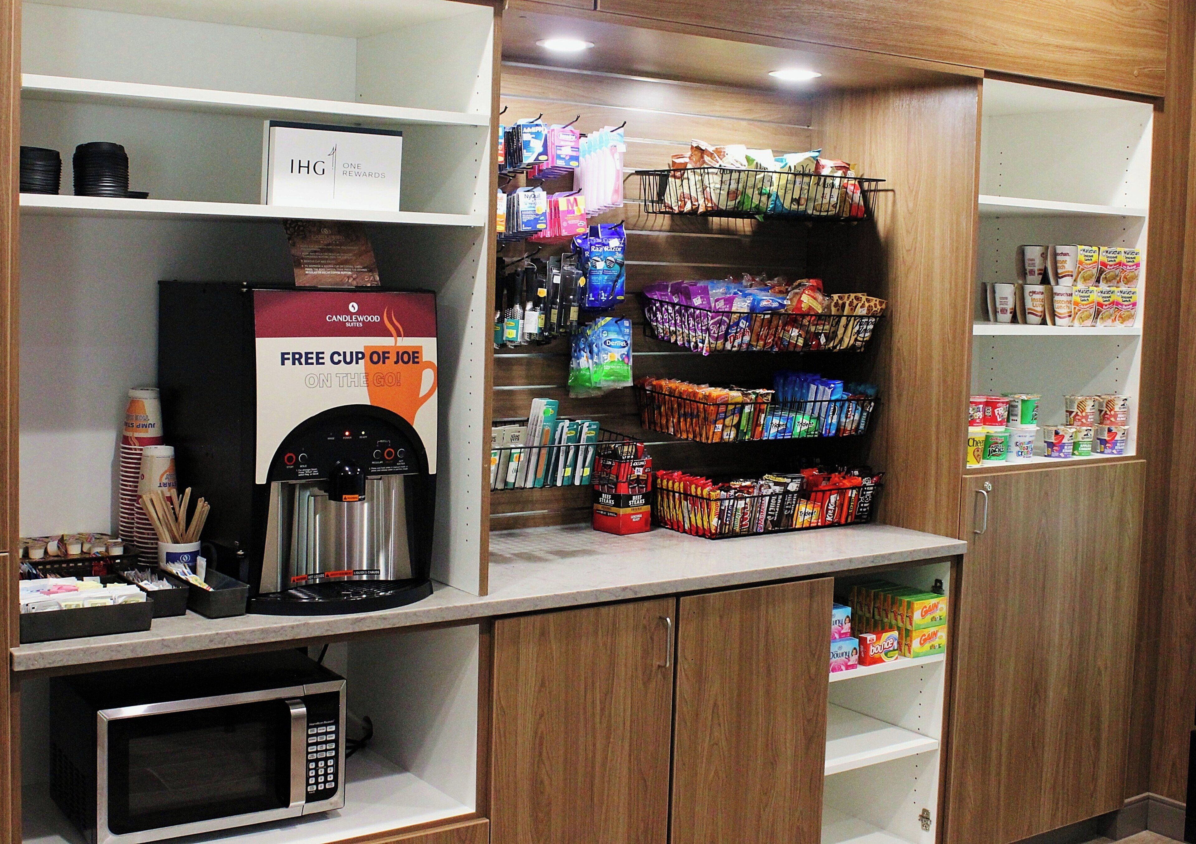 A kitchenette with a coffee machine, microwave, and various food items on shelves.