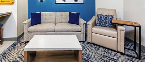 A living room with a sofa, armchair, coffee table, and a wall-mounted light fixture.