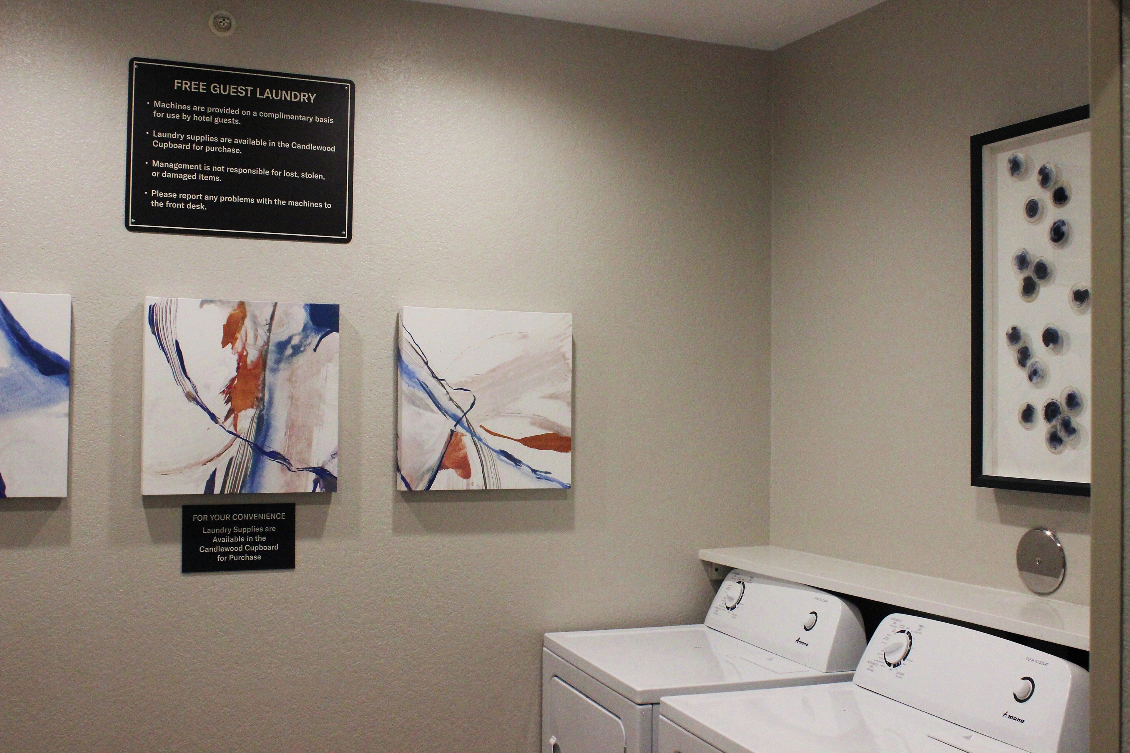 A laundry area with a sign indicating free guest laundry, a Candwood Cupboard for supplies, and two washing machines.