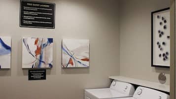 A laundry area with a sign indicating free guest laundry, a Candwood Cupboard for supplies, and two washing machines.