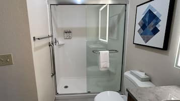 A compact bathroom with a glass-enclosed shower, a white toilet, and a marble countertop.