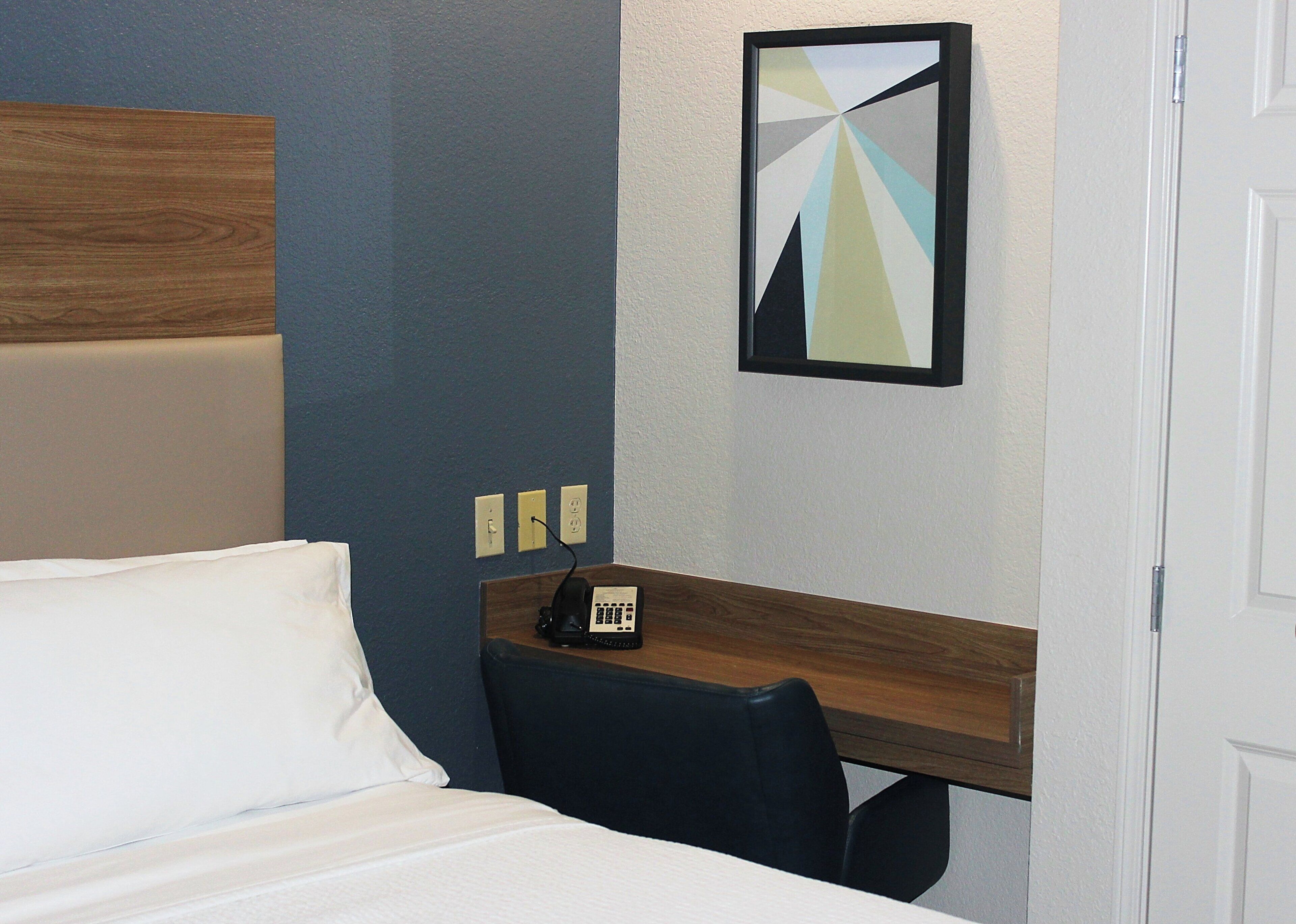 Ein Hotelzimmer mit Bett, Schreibtisch mit Telefon und einem Wandbild.