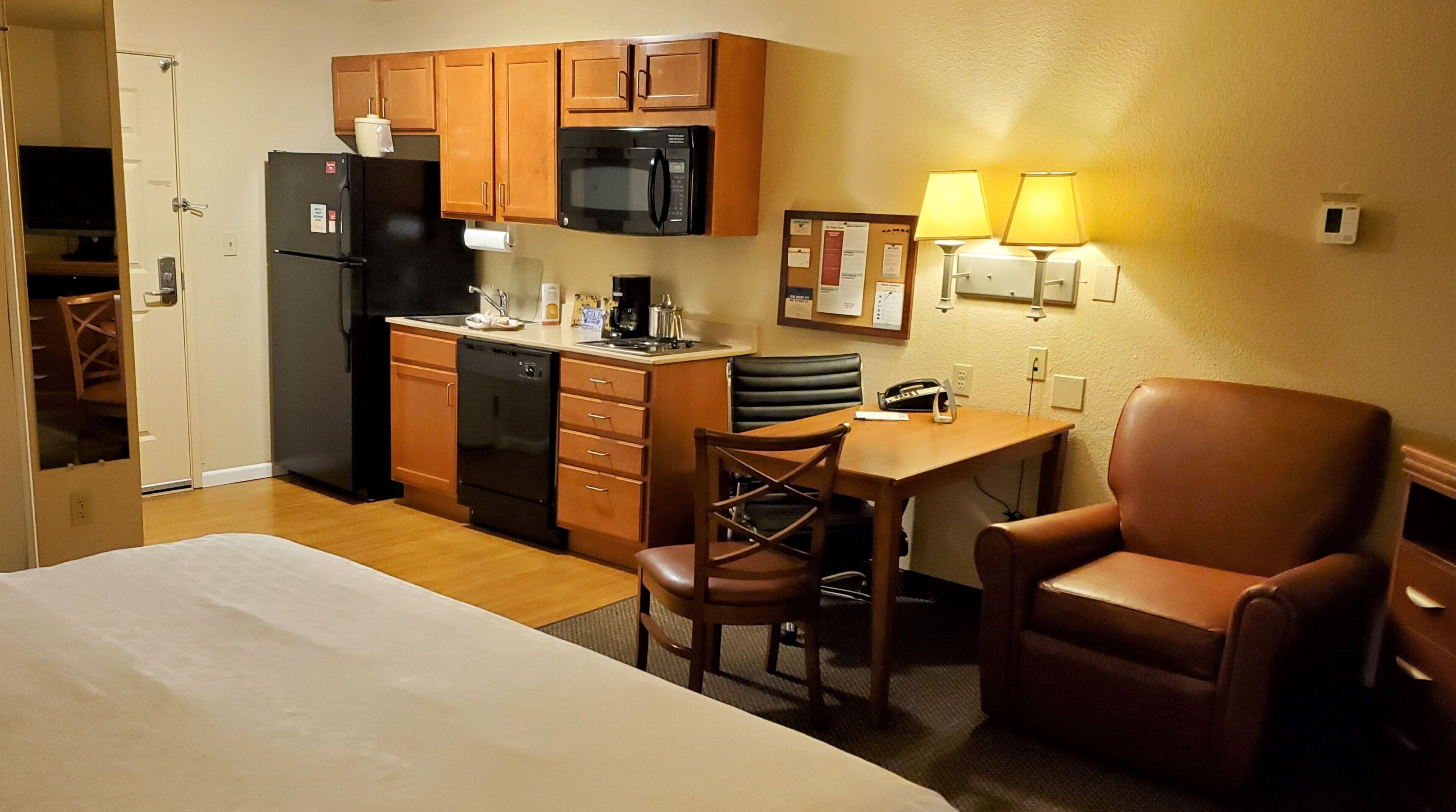 A hotel room with a bed, a desk with a chair, a microwave, a refrigerator, and a coffee maker.