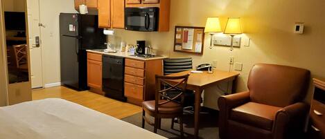 A hotel room with a bed, a desk with a chair, a microwave, a refrigerator, and a coffee maker.