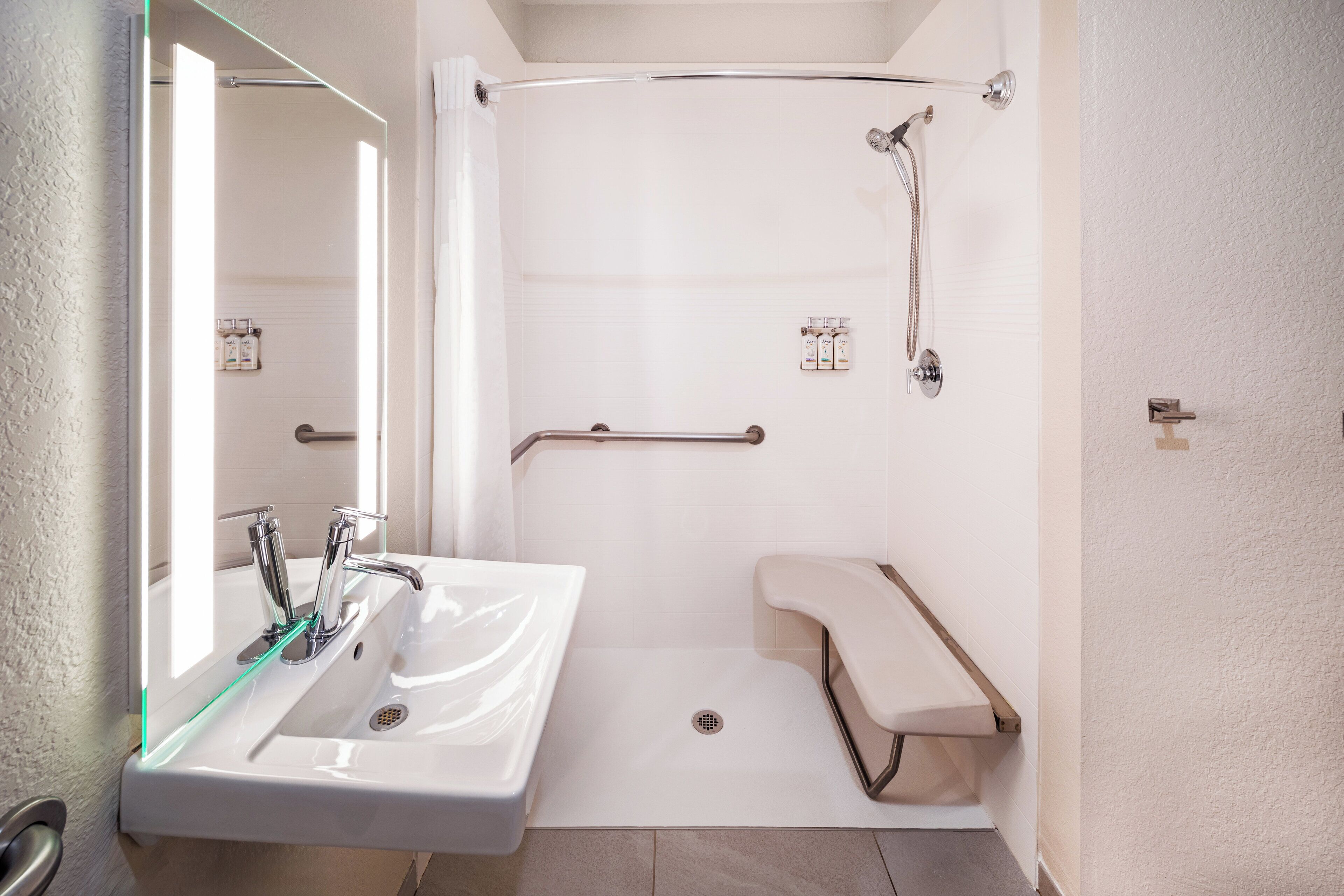 A modern bathroom with a white sink, a mirror, a shower with a glass door, and a grab bar.