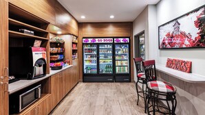 A kitchen area with wooden cabinets, a coffee machine, and a refrigerator stocked with beverages. There are two bar stools with checkered cushions.