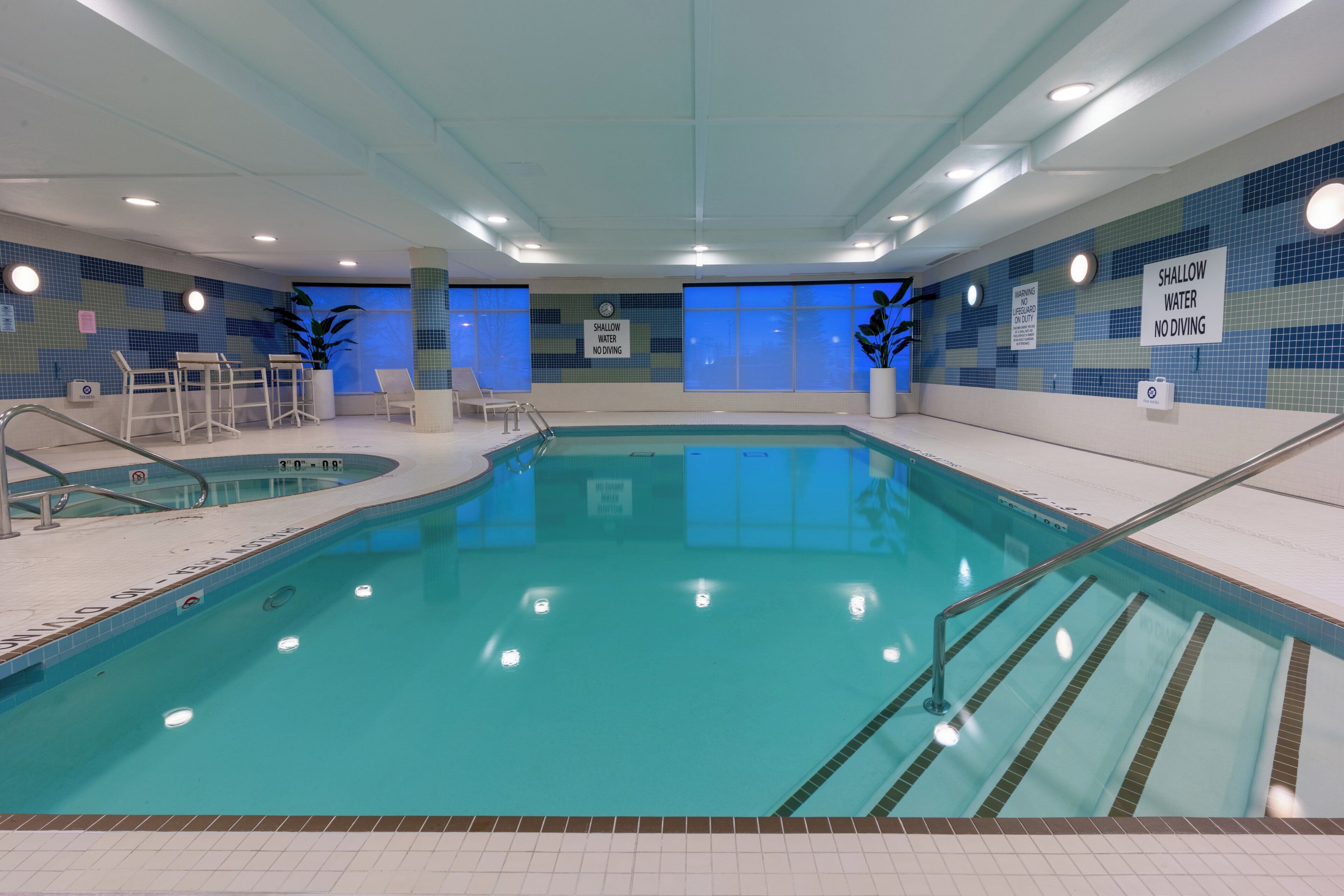 An indoor swimming pool with tiled walls, a sign indicating shallow water, and a lifeguard chair.
