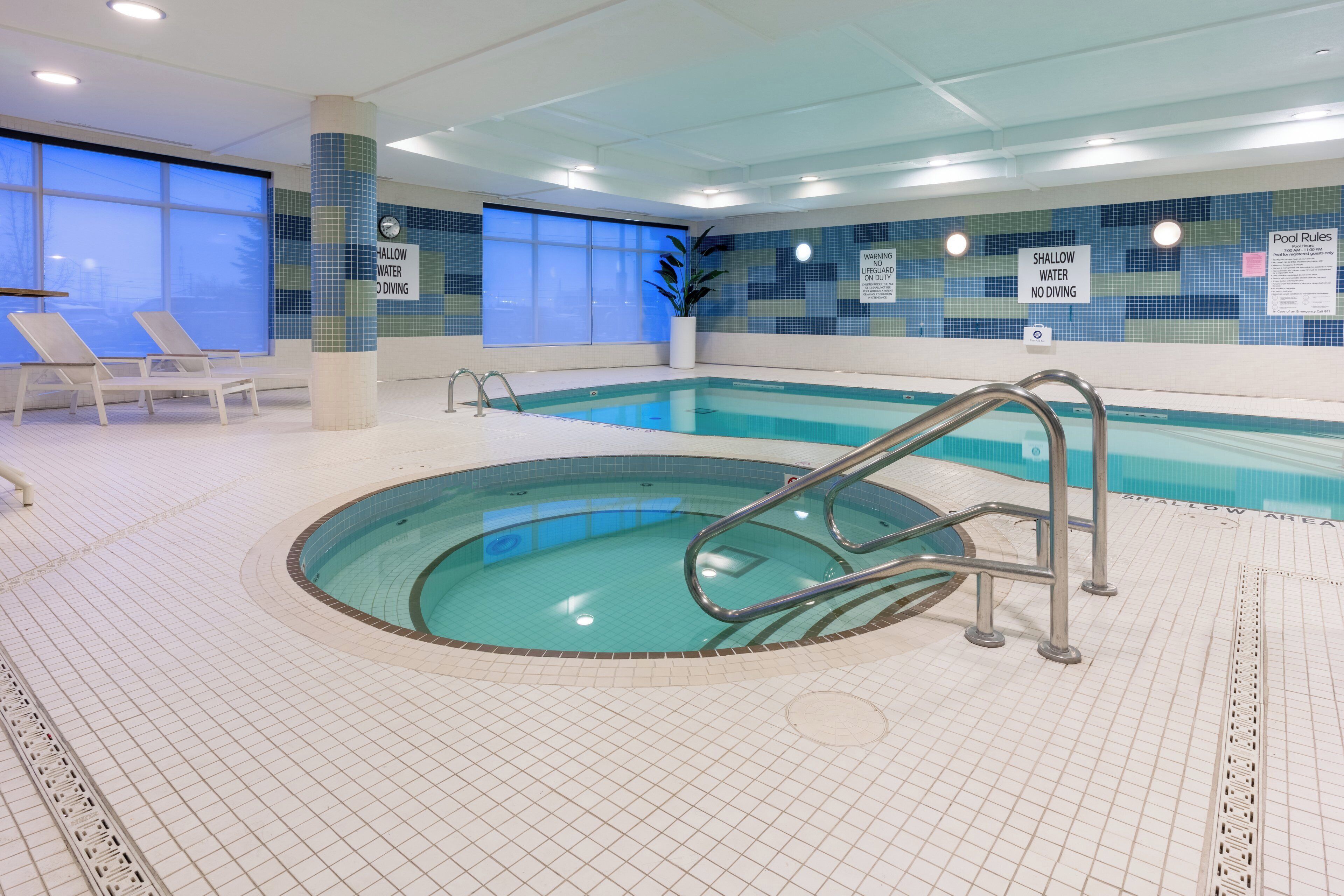 An indoor swimming pool with a shallow water area, lounge chairs, and a lifeguard on duty sign.