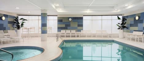 Una piscina interior con paredes de azulejos, sillas de descanso y un reloj en la pared.