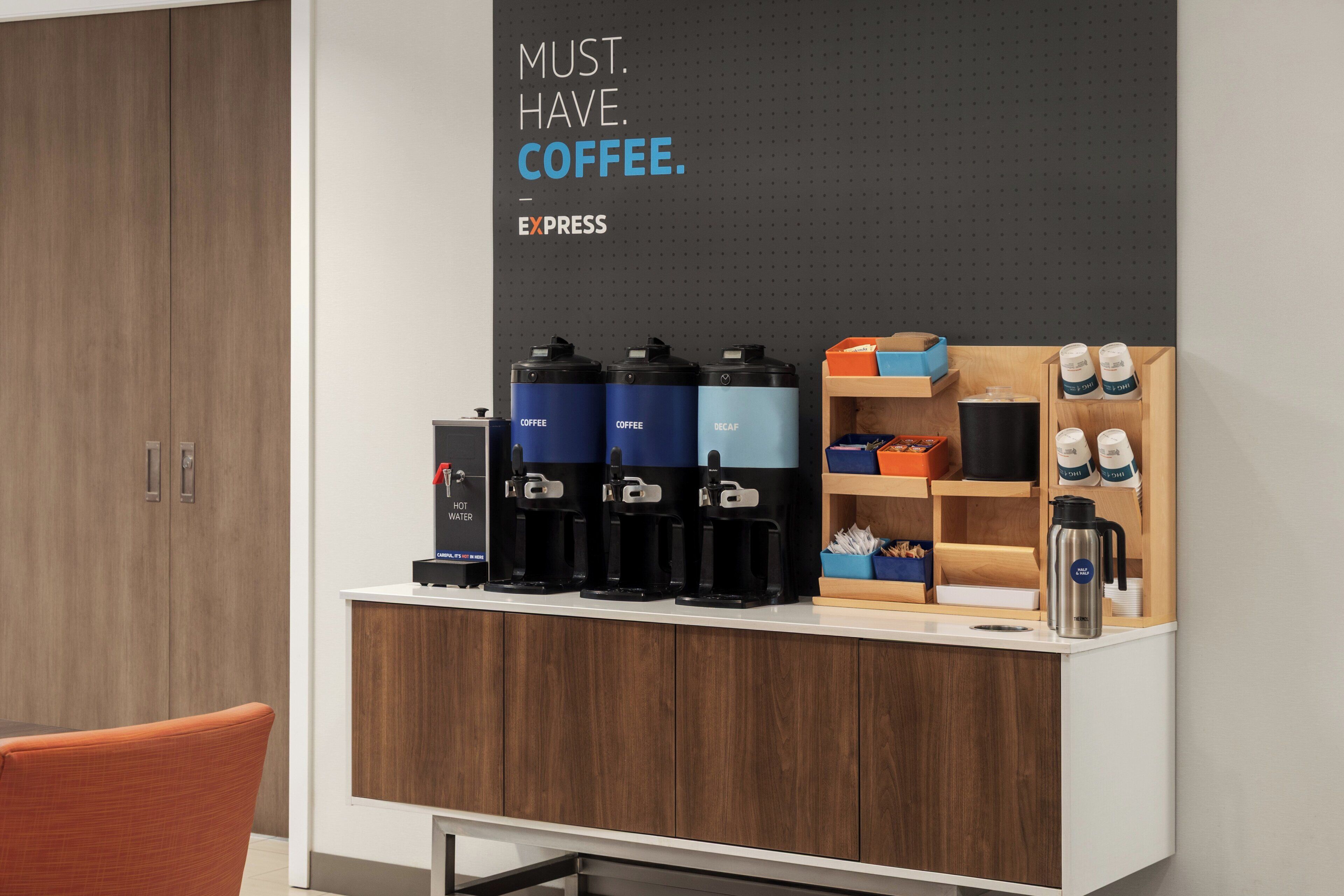 Un espace dédié au café, équipé de plusieurs distributeurs de café, d’un distributeur d’eau et d’une affiche sur le thème du café accrochée au mur.