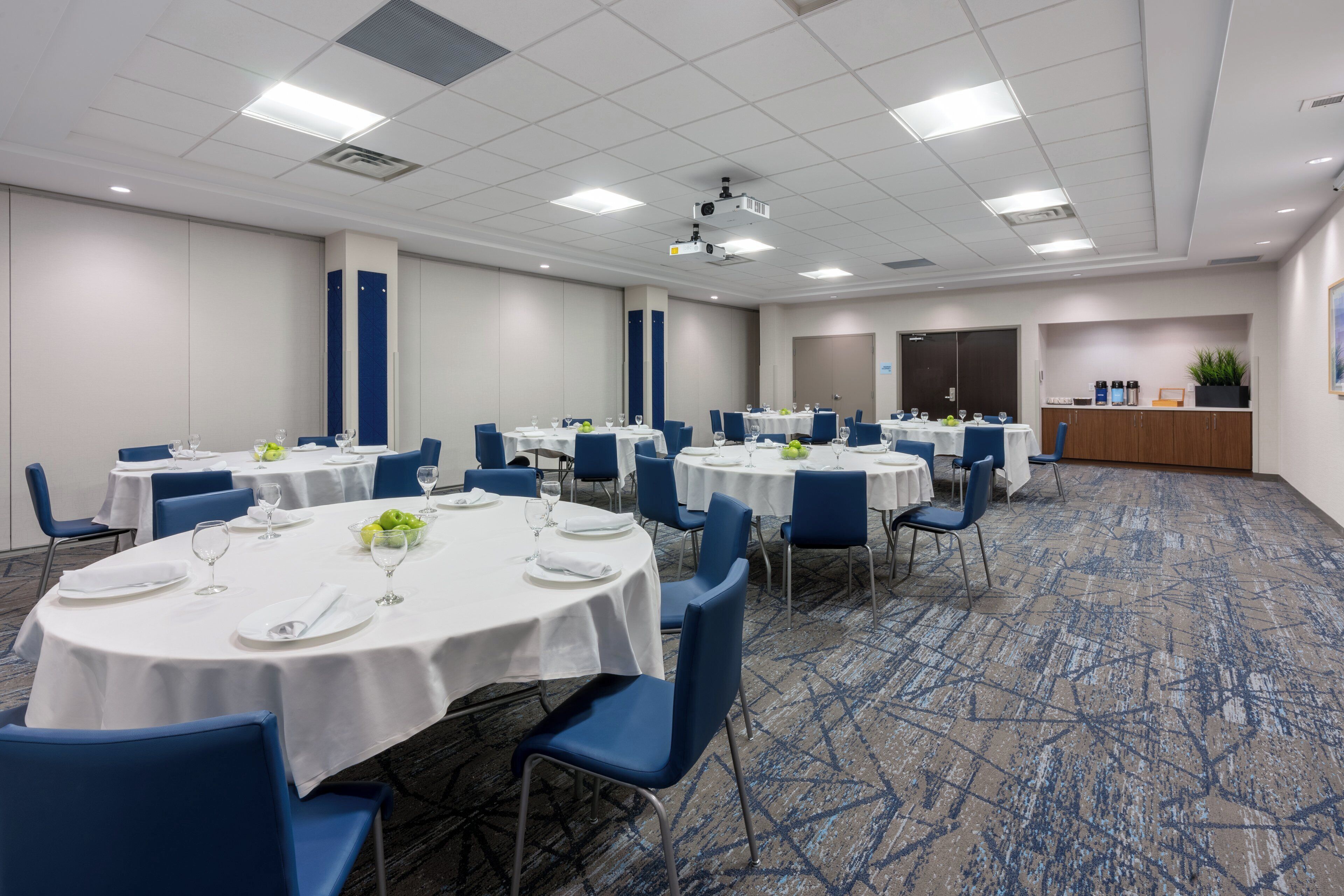 Un salón de conferencias con varias mesas redondas, sillas azules y manteles blancos.