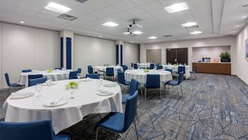 Un salón de conferencias con varias mesas redondas, sillas azules y manteles blancos.