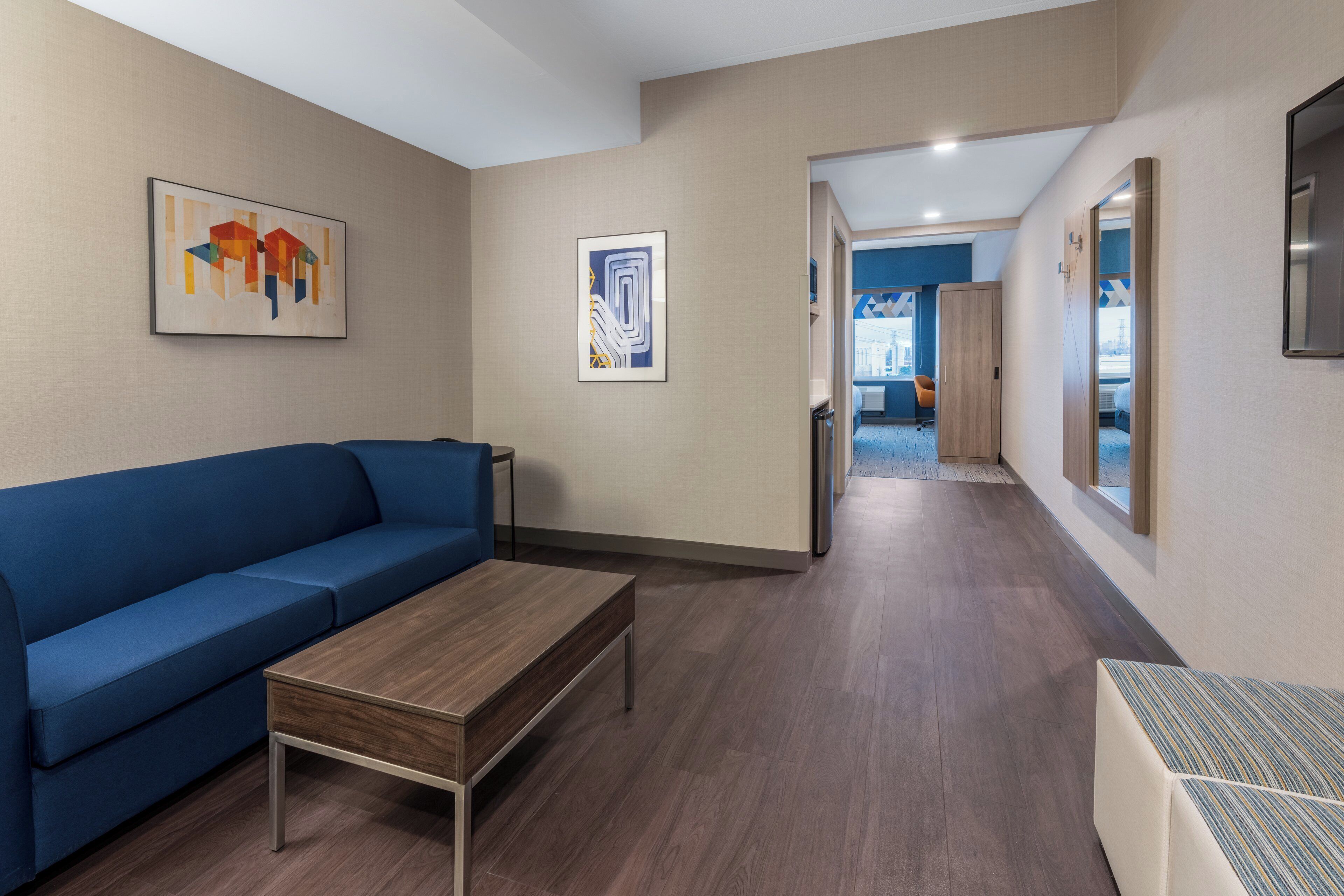 Habitación de hotel moderna con un sofá azul, una mesa de centro de madera y obras de arte en las paredes.