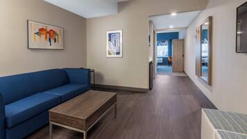 Habitación de hotel moderna con un sofá azul, una mesa de centro de madera y obras de arte en las paredes.